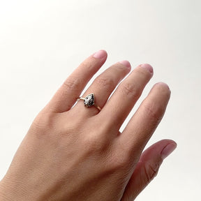 A narrow band 14k gold band that features a pear shaped rose cut salt and pepper diamond. The model wears the Ignis ring on their left hand ring finger as they rotate their hand from side to side. The Ignis ring is designed and handcrafted in Portland, Oregon.