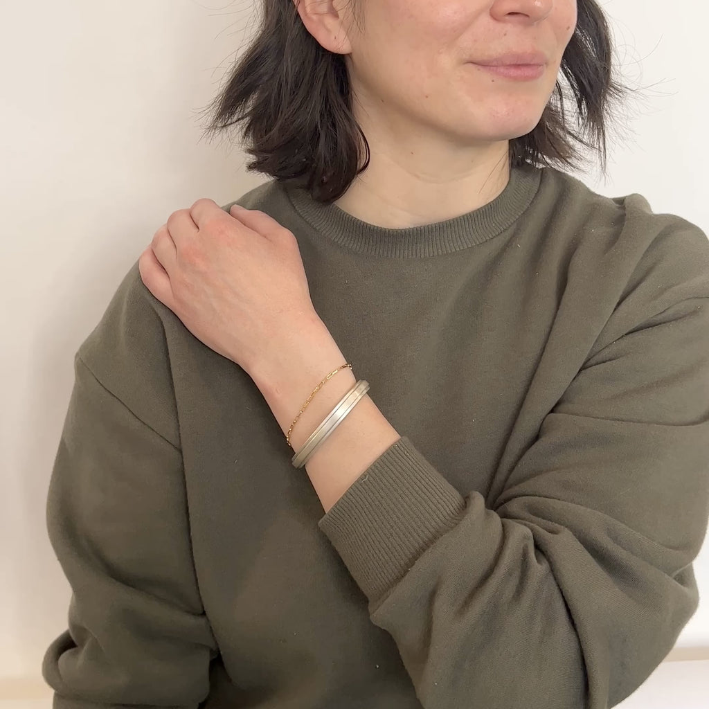 A model wears a squared off solid sterling silver cuff with an exterior band of silver running down the center. They turn their wrist from side to side. The Amanca Cuff is designed and handcrafted in Portland, Oregon.