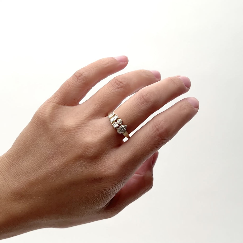 A 14k gold ring that features two lab grown baguette diamonds, and a lab grown square, round and marquis diamond, each in a bezel setting. Then Model wears the Astrum ring on their middle finger and rotates their hand form side to side. The Astrum ring is designed and handcrafted in Portland, Oregon.