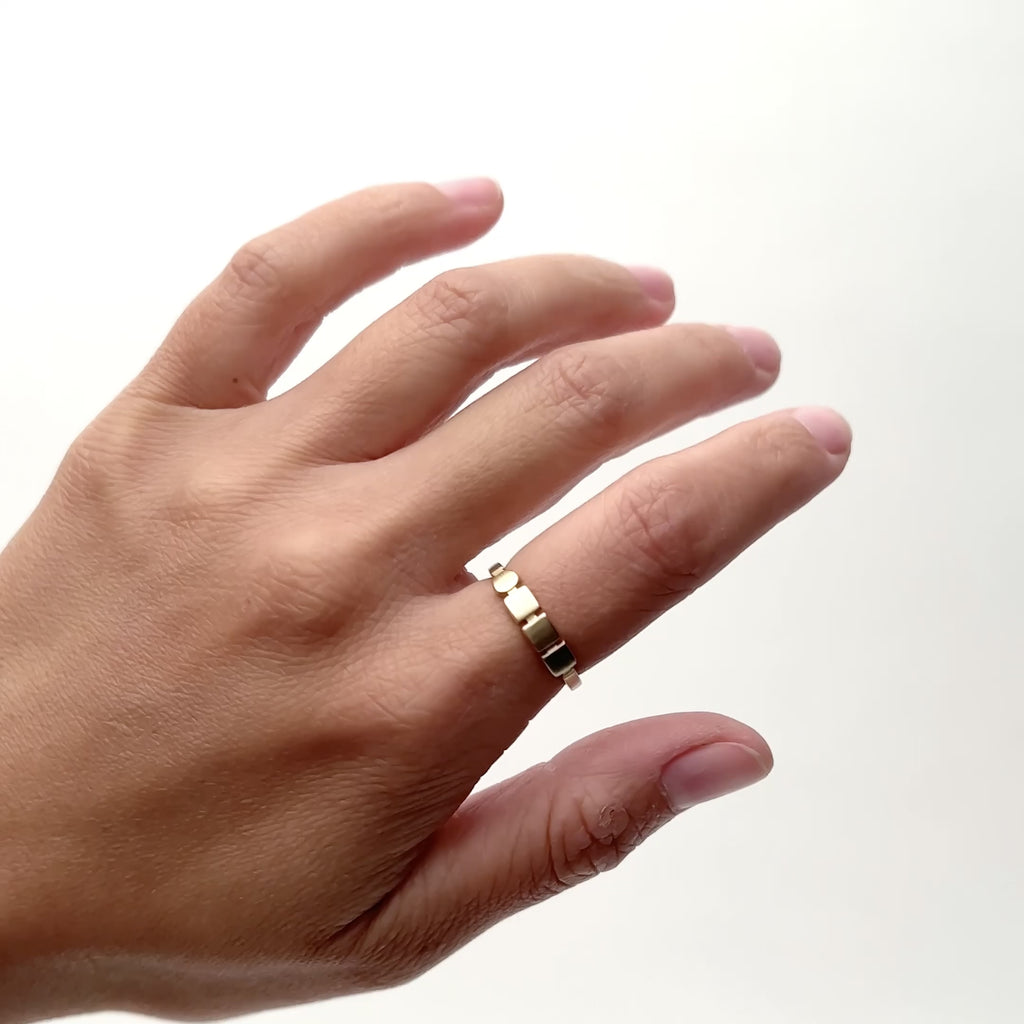 A model wears a semi narrow 14k gold band on their pointer finger. The band showcases a circle next to three square shapes that run horizontally in the band. Designed and handcrafted in Portland, Oregon.  