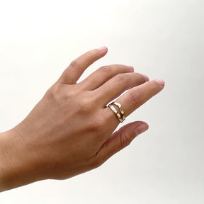 A model wears two narrow 14k yellow gold bands on their pointer finger. The south ring is a round band with seven petite round white diamonds set into the band (Aurum ring). The north band has a single round center stone flanked by two baguette diamonds. Designed and handcrafted in Portland, Oregon.