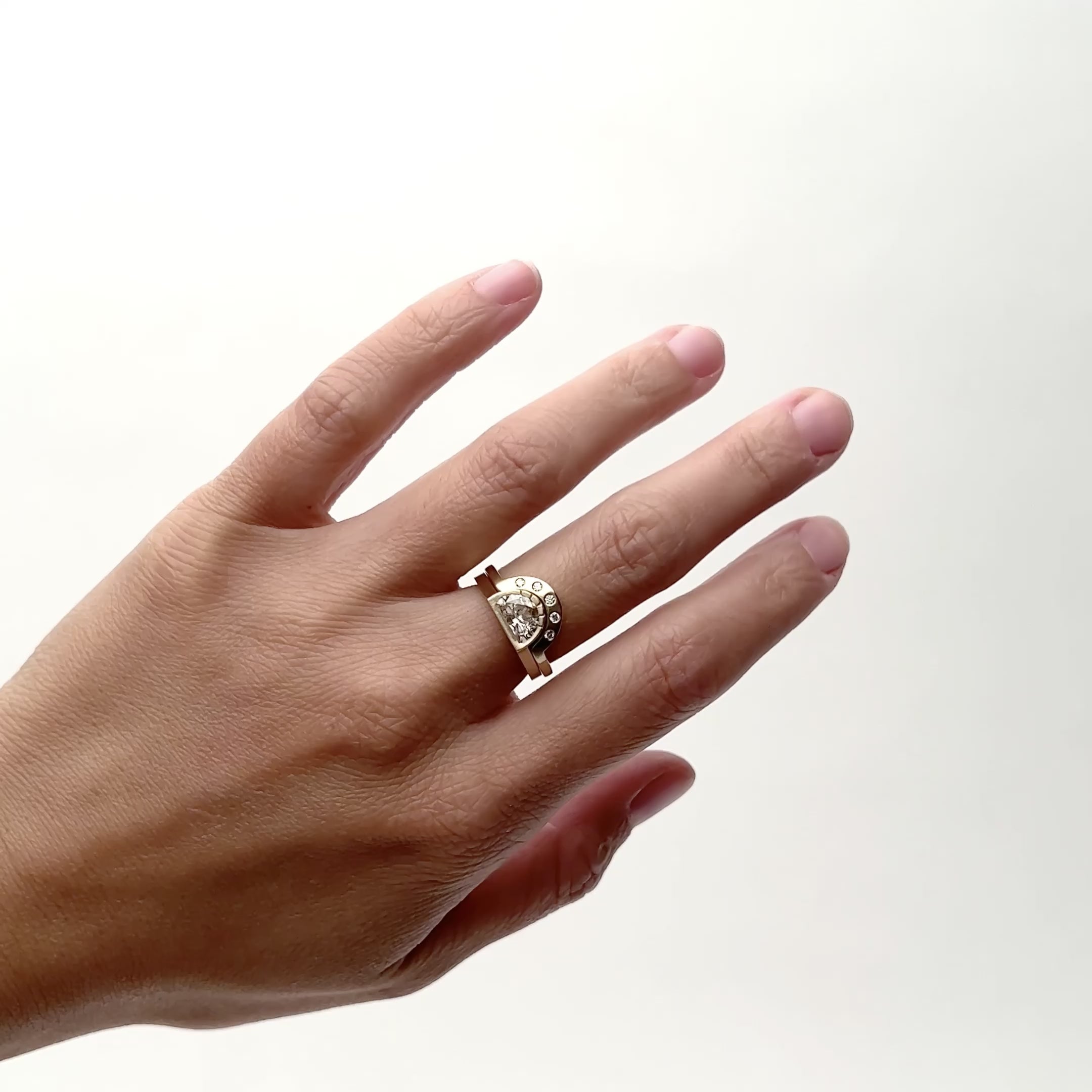A narrow 14k yellow gold ring featuring a bezel set lab grown white diamond in a semi-circle design. Five etched lines detail the round portion of the ring (Omnia ring). The flat, thin band stacks with the Omnia band and features five round black diamonds (Cor ring). Designed and handcrafted in Portland, Oregon.