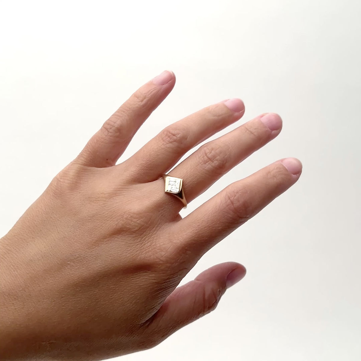 An offset square 14k gold ring with a square patchwork of white baguette diamonds. The model rates their hand from side to side with the ring on the middle finger. The Elicio ring is designed and handcrafted in Portland, Oregon.