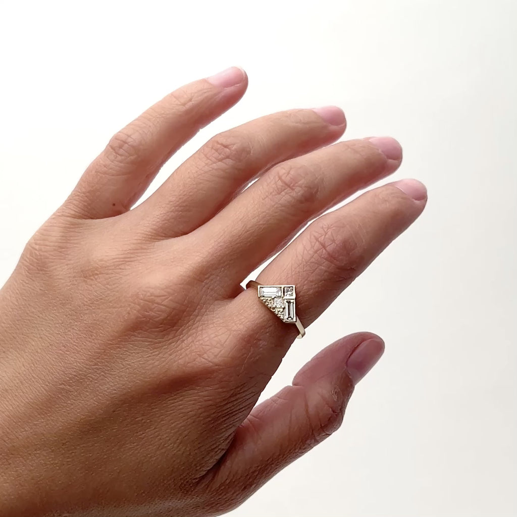 A model wears a triangle shaped ring with a flat surface. The surface features two square cut diamonds, two baguette shaped diamonds and 6 petite round cut diamonds, all of which are set in a narrow 14k gold band. Designed and handcrafted in Portland, Oregon.