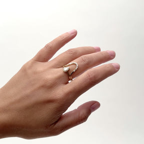 A model wears a narrow curved 14k gold ring on their middle finger. Set in the ring are seven petite round diamonds. Flanking the setting of round diamonds is a baguette white diamond. The Levo ring sits with a pear shaped white diamond ring. Designed and handcrafted in Portland, Oregon.