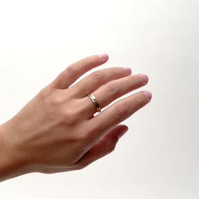 A model wears two thin 14k gold bands. The south band features a petite round lab grown white diamond (Vis ring). The north ring features a white diamond baguette on one side a round black diamond set on the other with a space in the center of the ring (Manus ring). Designed and handcrafted in Portland, Oregon.