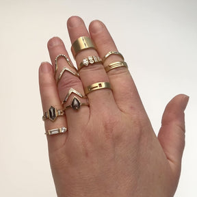 A model wears a wide band gold ring on the end of their middle finger. This ring features a vertical setting of lab grown white diamonds and a slight curvature on the top and bottom of the band. Pinky finger: Otium ring and Libero ring. Ring finger: Ignis ring, Altus ring (polished), Altus ring (matte), Levo ring. Middle finger: Sero ring, Laetus ring, Decus ring. Pointer finger: Vitae ring and Basio ring (black diamond).
