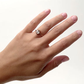 A narrow band 14k gold ring with a rounded rose cut salt and pepper diamond. The diamond is clasped by two arch shaped prongs and sits on an a base of gold with curved etchings and a cut out on the north and south sides. The model wears the Caelus ring on their left hand ring finger. The Caelus ring is designed and handcrafted in Portland, Oregon.