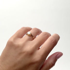 A model wears a 0.7 ct. diamond ring on their ring finger. The diamond is round and bezel set in 14k gold. The band is rounded and a wall of gold surrounds the sides of the diamond. Designed and handcrafted in Portland, Oregon.