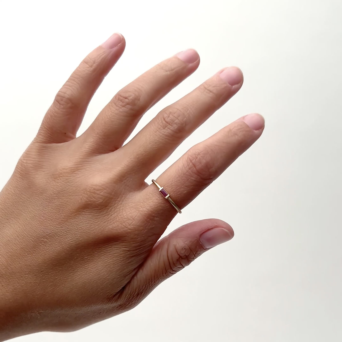 A model wears an ultra thin 14k yellow gold rounded band with a Ruby baguette set into the center. Designed and handcrafted in Portland, Oregon.