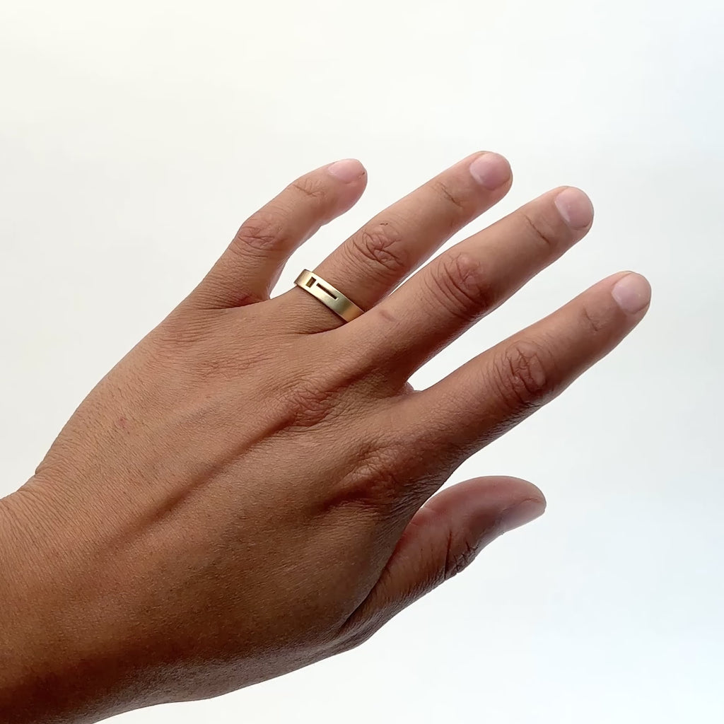 A model wears a semi narrow 14k gold ring. A square and a line are cut out from  the face of the ring. Designed and handcrafted in Portland, Oregon.