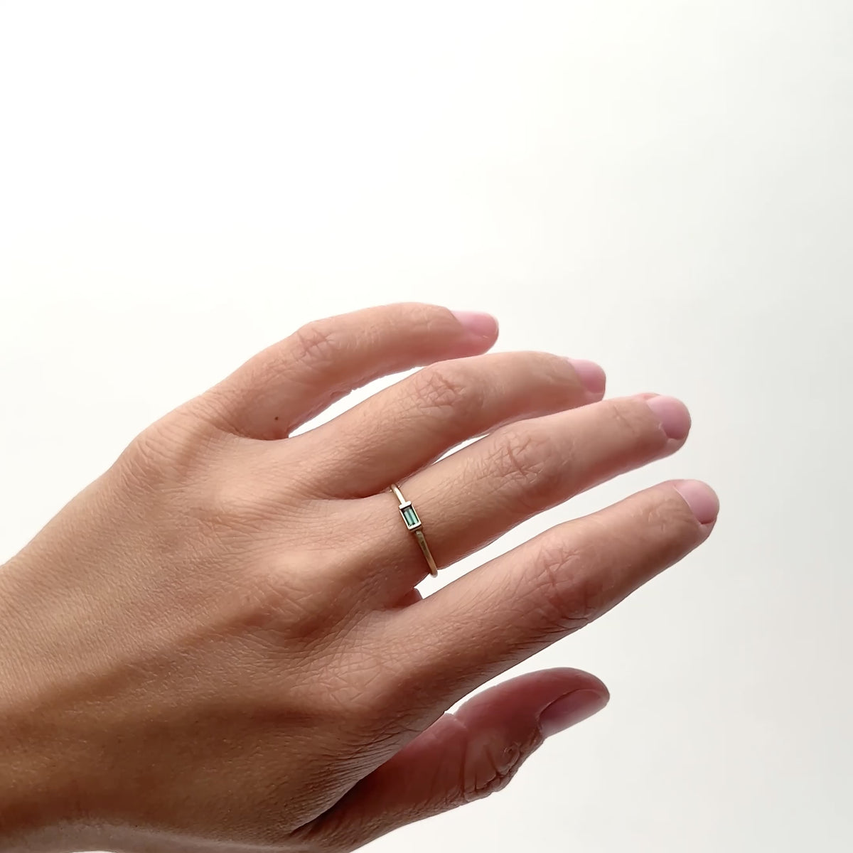 A model wears an ultra thin 14k yellow gold rounded band with a Tourmaline baguette set into the center. Designed and handcrafted in Portland, Oregon.
