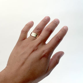 A model wears a wide band 14k gold ring in a polished finished with delicate line etchings on their ring finger. On the north of the ring is a narrow 14k gold band (Amandi ring) with half circle etchings. Designed and handcrafted in Portland, Oregon.