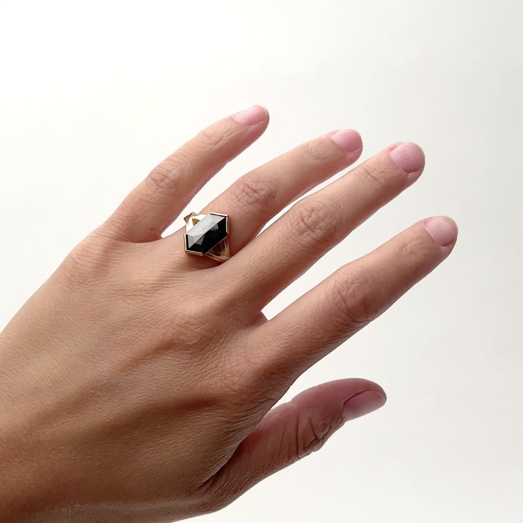 A model wears a large hexagon shaped salt and pepper diamond set in 14K gold. The band features a Y shaped shank design with a raised gold strip in the center of the band. Designed and handcrafted in Portland, Oregon.