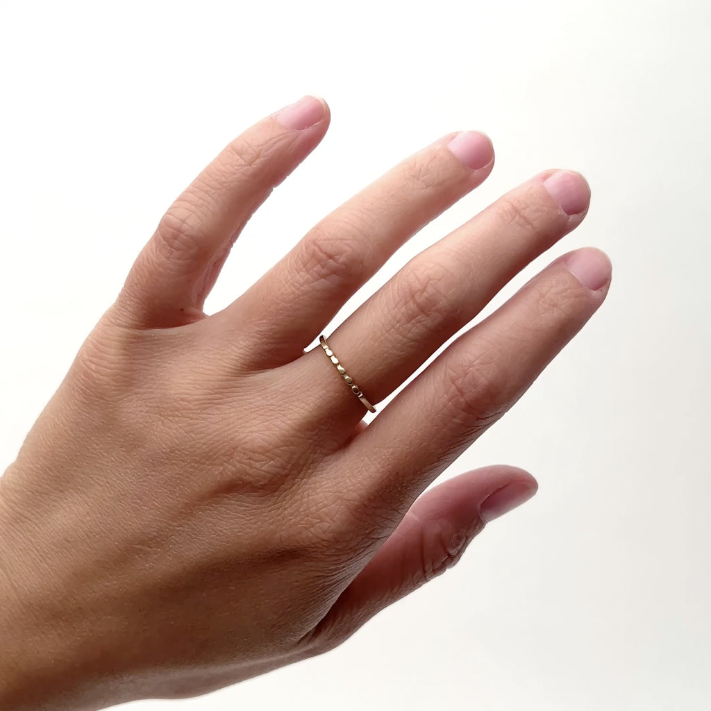 A model wears a narrow 14k gold band on their middle finger. The ring features five circular shapes along the face of the band. Designed and handcrafted in Portland, Oregon.