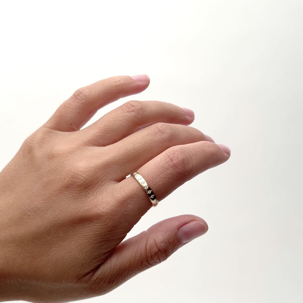 A model wears a semi-narrow 14k gold band with a rounded face. Set into the band are seven petite round diamonds. On the north and south of each diamond is a small etched line. Designed and handcrafted in Portland, Oregon.