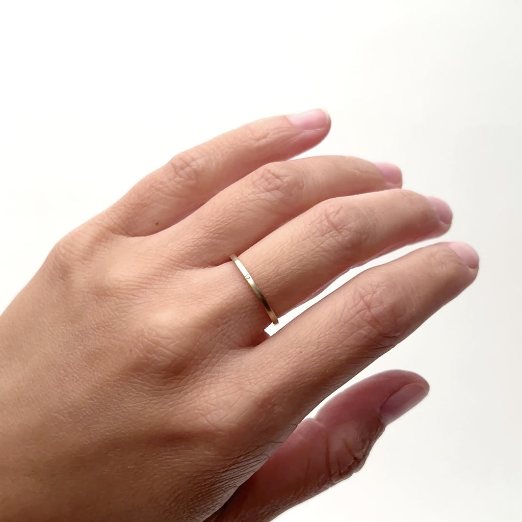 A model wears a flat, ultra thin 14k yellow gold band on their middle finger. The band as a petite lab grown white diamond in the center. Designed and handcrafted in Portland, Oregon. 