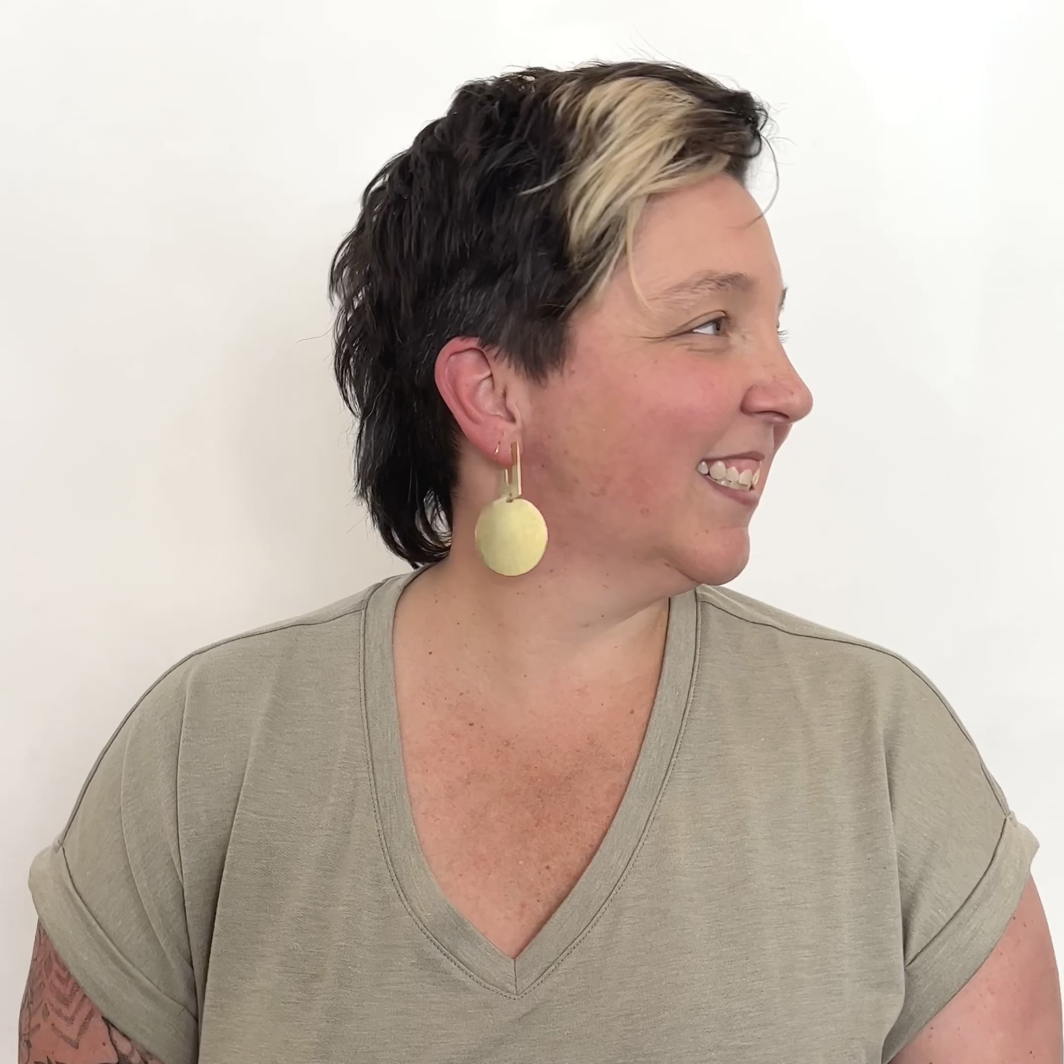 A model wears a squared off u-shaped stud earring connected with a large hammered circular disk. They turn their head from right to left to show its movement. The Candetta earrings are designed and handcrafted in Portland, Oregon.