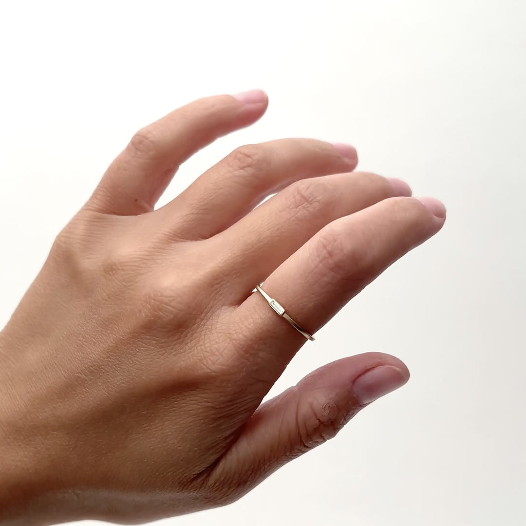 A model wears an ultra thin 14k yellow gold band with a single white diamond baguette set into the center. Designed and handcrafted in Portland, Oregon.