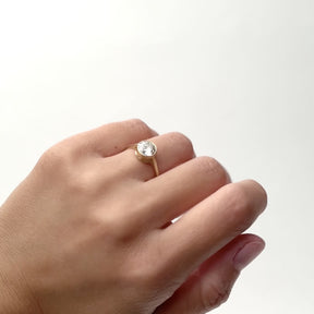 A model wears a 14k yellow gold ring with a 1.4ct. Round lab grown white diamond. On the north and south sides of the setting are two petite round white diamonds. The gold band consists of a split shank design. Designed and handcrafted in Portland, Oregon.