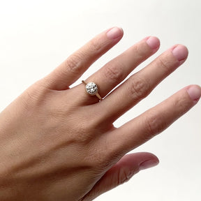 A model wears a 1.3 ct. diamond ring on their ring finger. The diamond is round and bezel set in 14k gold. The band is rounded and a wall of gold surrounds the sides of the diamond. Designed and handcrafted in Portland, Oregon.