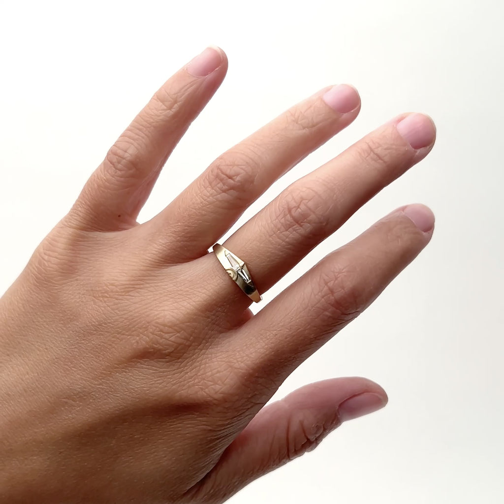 A model wears a 14k yellow gold band on their middle finger. The band widens in the middle and forms a slight peak. Set in the band are two baguette diamonds. The south portion of the face features etched half circles. Designed and handcrafted in Portland, Oregon.