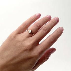 A model wears a narrow 14k yellow gold band with a bezel set .5ct pear shaped lab grown white diamond set in the center. The round portion of the setting features a cut-out. Designed and handcrafted in Portland, Oregon.