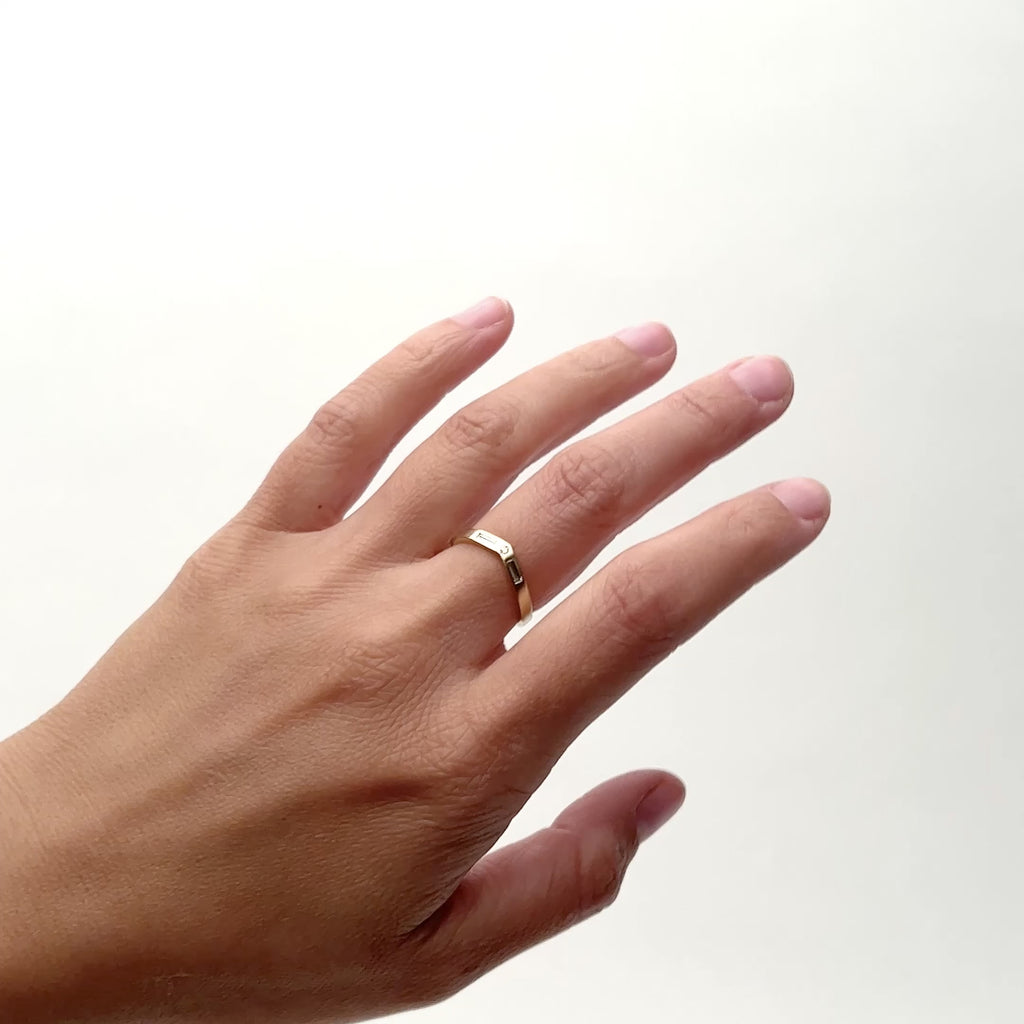 A model wears a narrow band 14k yellow gold band with a slight peak shape on the middle finger. Set in the center is one round diamond flanked by two baguette diamonds. Designed and handcrafted in Portland, Oregon.