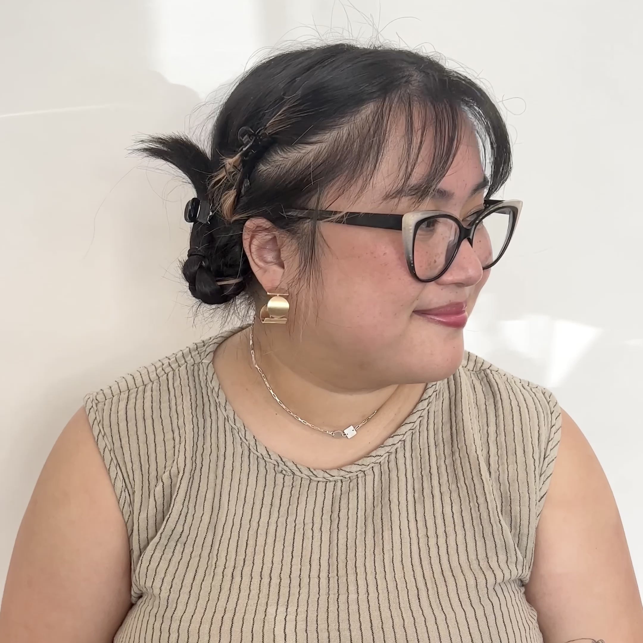 A model wears a wide band bronze hoop earring featuring a circular and rectangular pattern. The move their head to the side to and smile. Designed and handcrafted in Portland, Oregon.