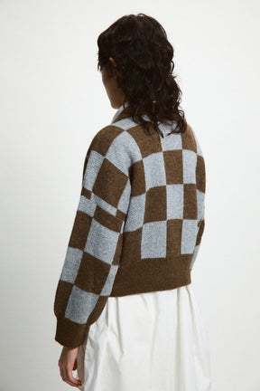 A model shows the backside of a knitted cardigan in a blue and brown checkerboard pattern. The Ellen Sweater in Brown + Blue is designed by Rita Row and made in Girona, Spain.