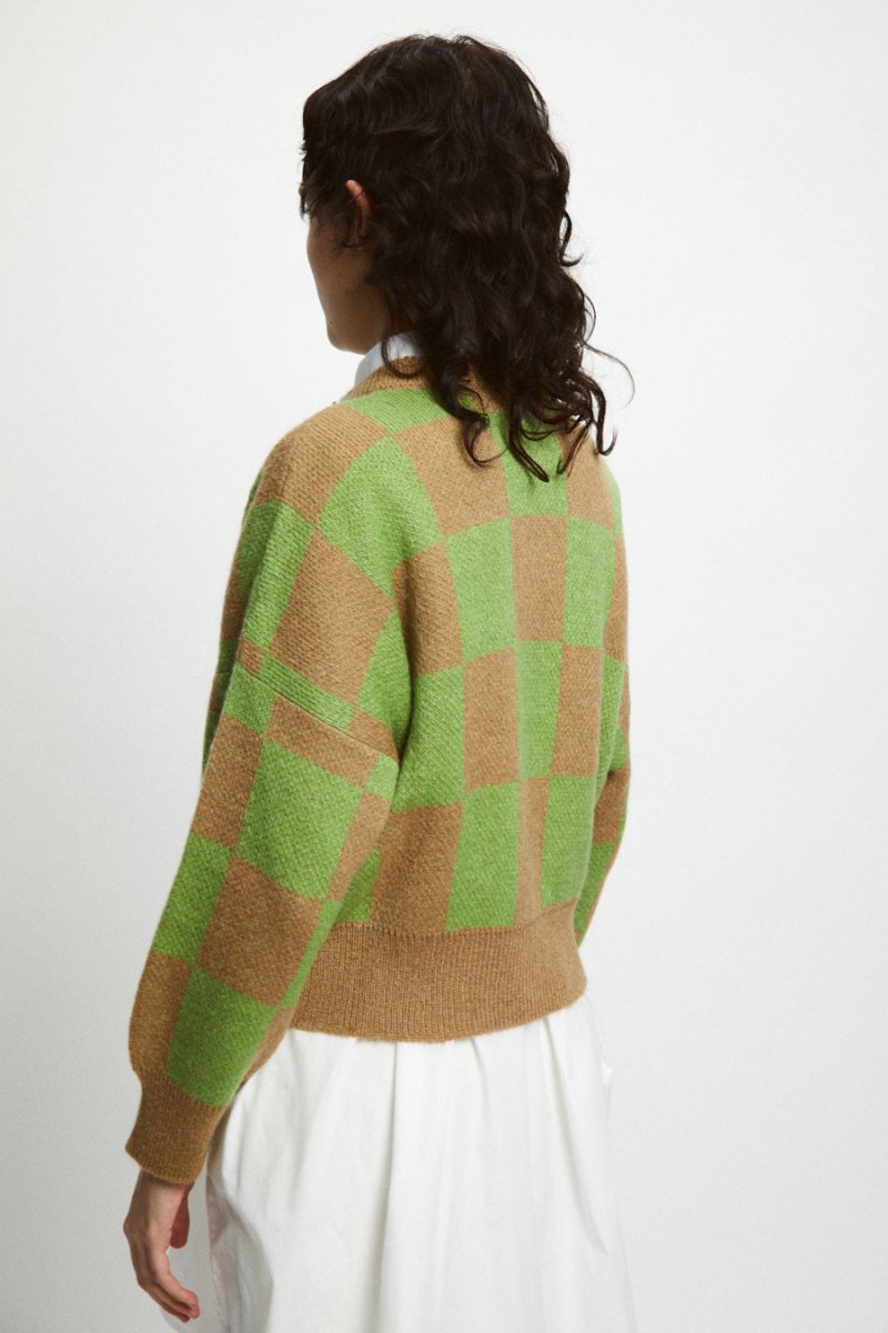 A model shows the back side of a knitted button up cardigan in a light brown and green checkerboard pattern. The Ellen Sweater is designed by Rita Row and made in Girona, Spain.