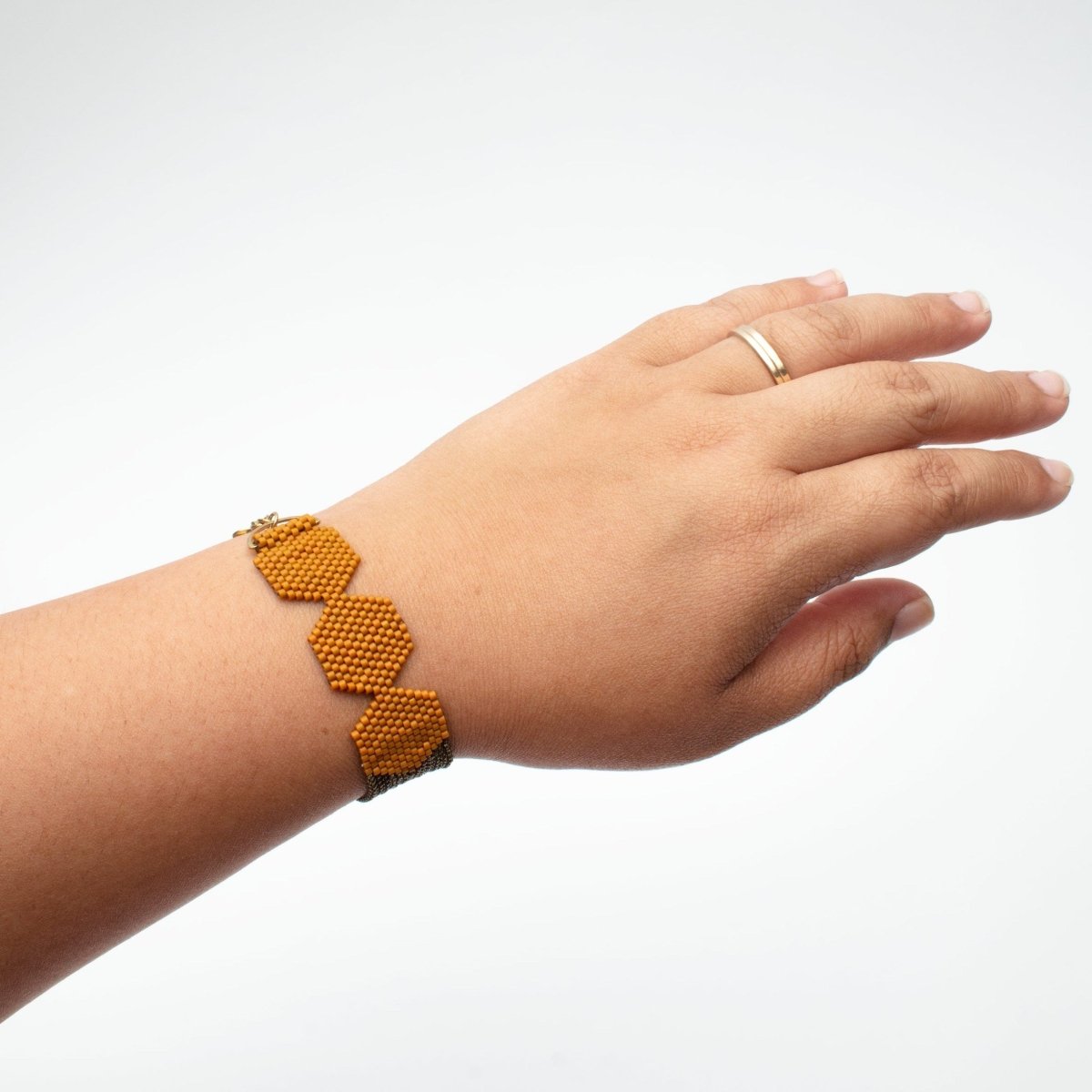 A model wears a hexagon beaded bracelet made with burnt orange colored beads and antique brass chains. The Row Bracelet in Toast is designed and handmade by A Nod To Design in Portland, OR.