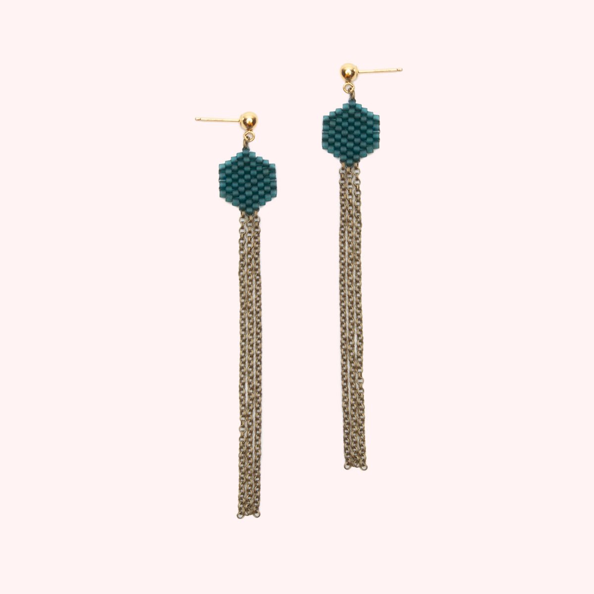A gold-fill stud earring holds a small beaded hexagon in a jewel tone teal color. A narrow collection of antiqued brass chain hangs from the beaded portion. The Dot Earrings in Teal are designed and handcrafted by A Nod to Design in Portland, OR.