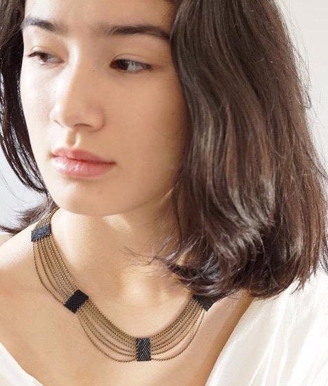 The Eternity Necklace made with antique brass chains and black Japanese Miyuki Delica beads. Worn on a model with dark brown hair. Handmade by A Nod To Design in Portland, OR.
