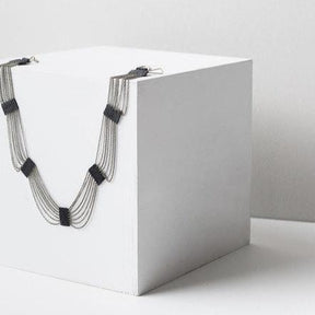 The Eternity Necklace made with antique brass chains and black Japanese Miyuki Delica beads, draped over a white box against a white background. Handmade by A Nod To Design in Portland, OR.