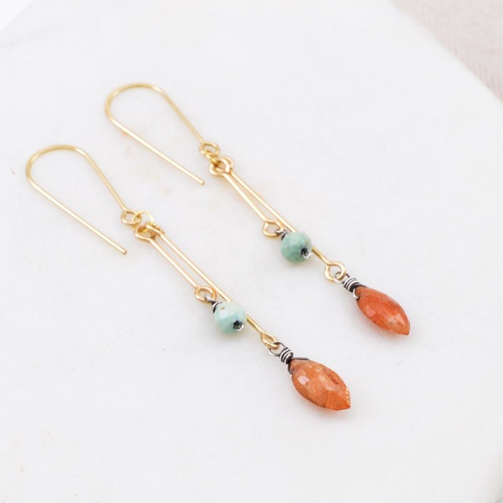 A spheroid faceted sunstone hangs from a gold-fill bar along with a teal turquoise stone. The Adelaide Earrings re designed and handcrafted by Amy Olson in Portland, Oregon.