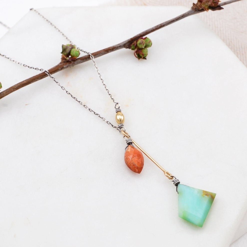 A geometrically cut teal opal hangs from a gold-fill bar attached to a faceted orange spheroid shaped sunstone. The Adelaide Necklace is designed and handcrafted by Amy Olson in Portland, Oregon.