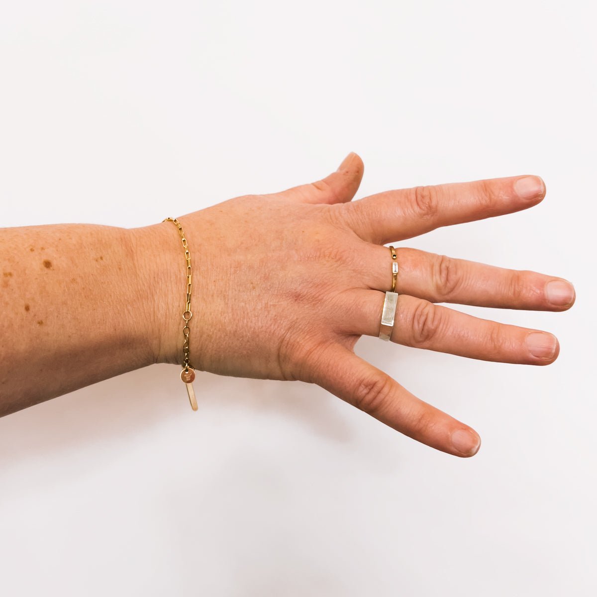 A model wears a delicate gold fill chain link bracelet with two petite rectangular tags, lobster clasp and jump rings to allow for adjustability. The Alba Bracelet is designed and handcrafted in Portland, Oregon.