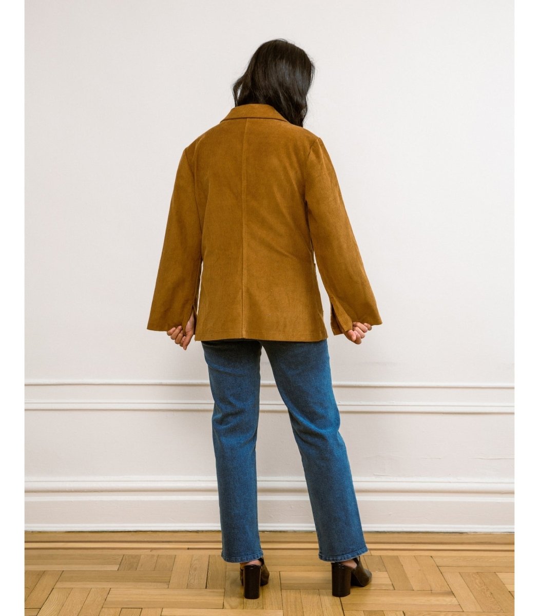 A model shows the backside of a tan corduroy jacket and wide sleeves. The Angelica Jacket in Chestnut Cord is designed from Loup and made in New York City, USA.