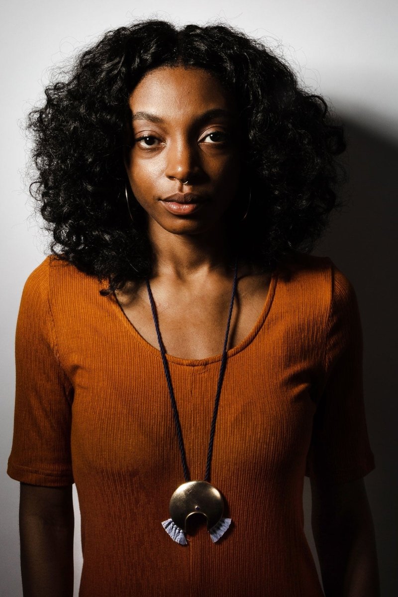 The bronze Animo necklace, with periwinkle fringe and navy blue cotton cord, worn long on a model with an ochre dress and large betsy & iya Unda hoop earrings.