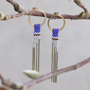 Two brass circle stud earrings with cascading antique brass chains and delicate beadwork in blue, white and red. The Avant Earrings in Royal Blue are designed by A Nod to Design and handmade in Portland, OR.