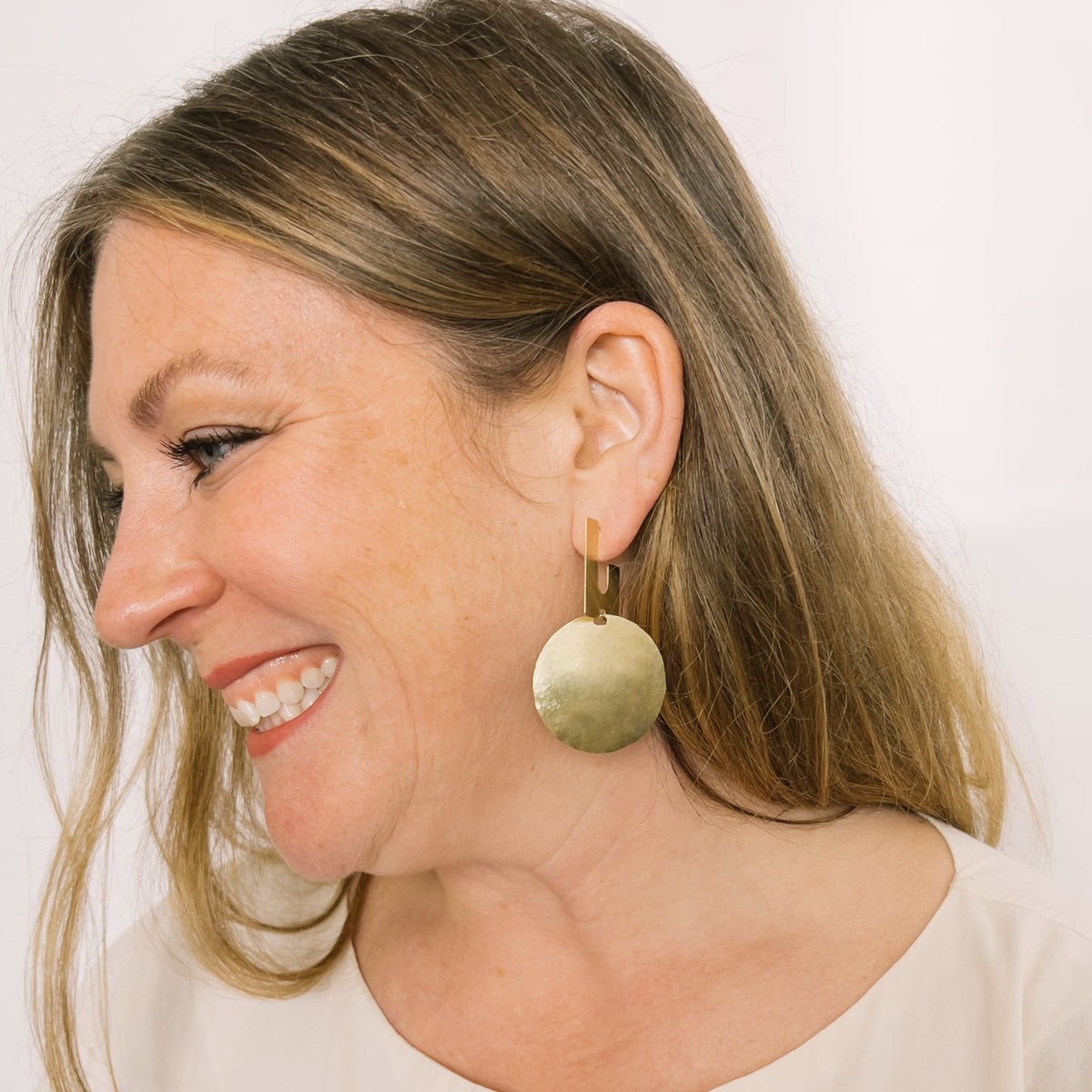 A model wears a squared off u-shaped stud earring connected with a large hammered circular disk. The Candetta Earrings are designed and handcrafted in Portland, Oregon.