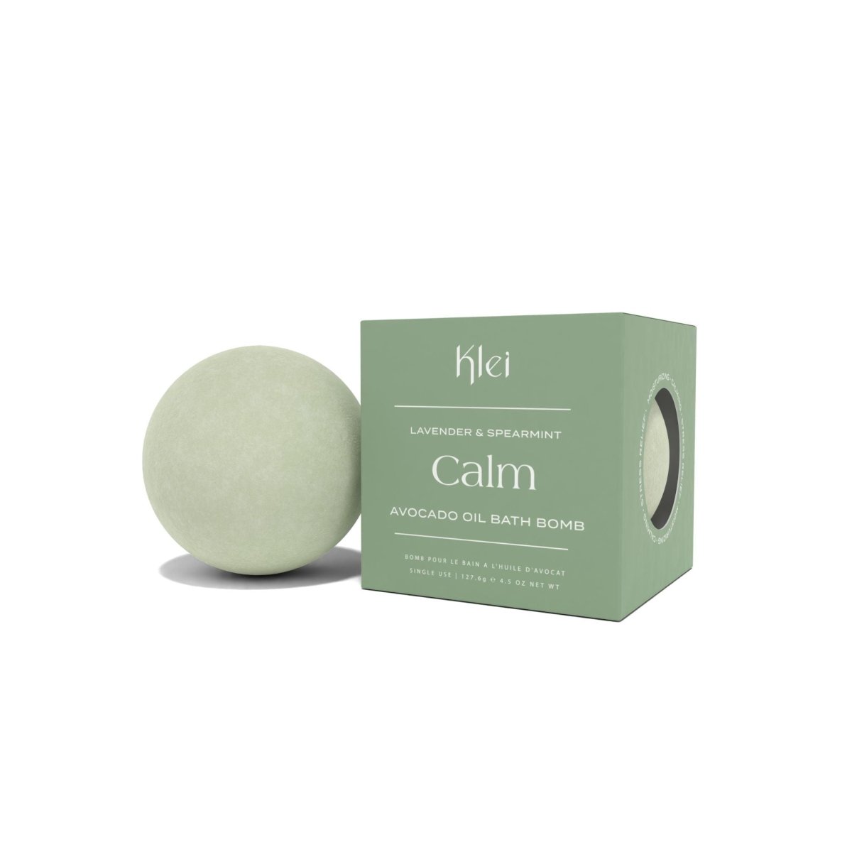 A light green bath bomb leans against a green box against a white background. The Lavender & Spearmint Avocado Bath Bomb is formulated by Klei Beauty and manufactured in New Jersey, USA.