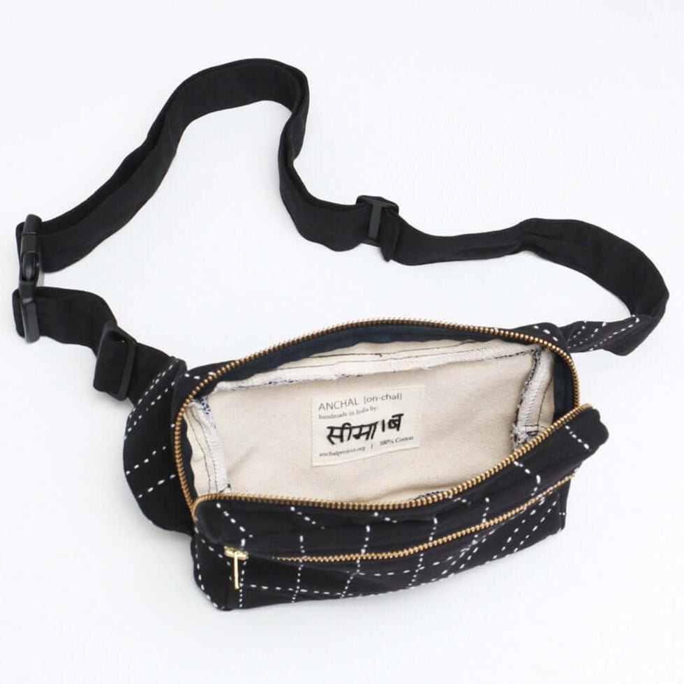 A black crossbody bag with white stitched detail and open zipper to show interior. The Crossbody Belt Bag in Charcoal is designed by Anchal in Louisville, KY and handmade in Ajmer, India.
