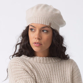 Model wears a slouch style hat with fitted ribbed collar. The Merino Beret in Almond White is designed by Dinadi and hand knitted in Kathmandu, Nepal.