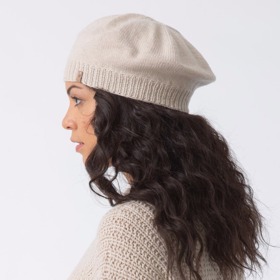Model shows the side profile of a slouch style hat with fitted ribbed collar. The Merino Beret in Almond White is designed by Dinadi and hand knitted in Kathmandu, Nepal.