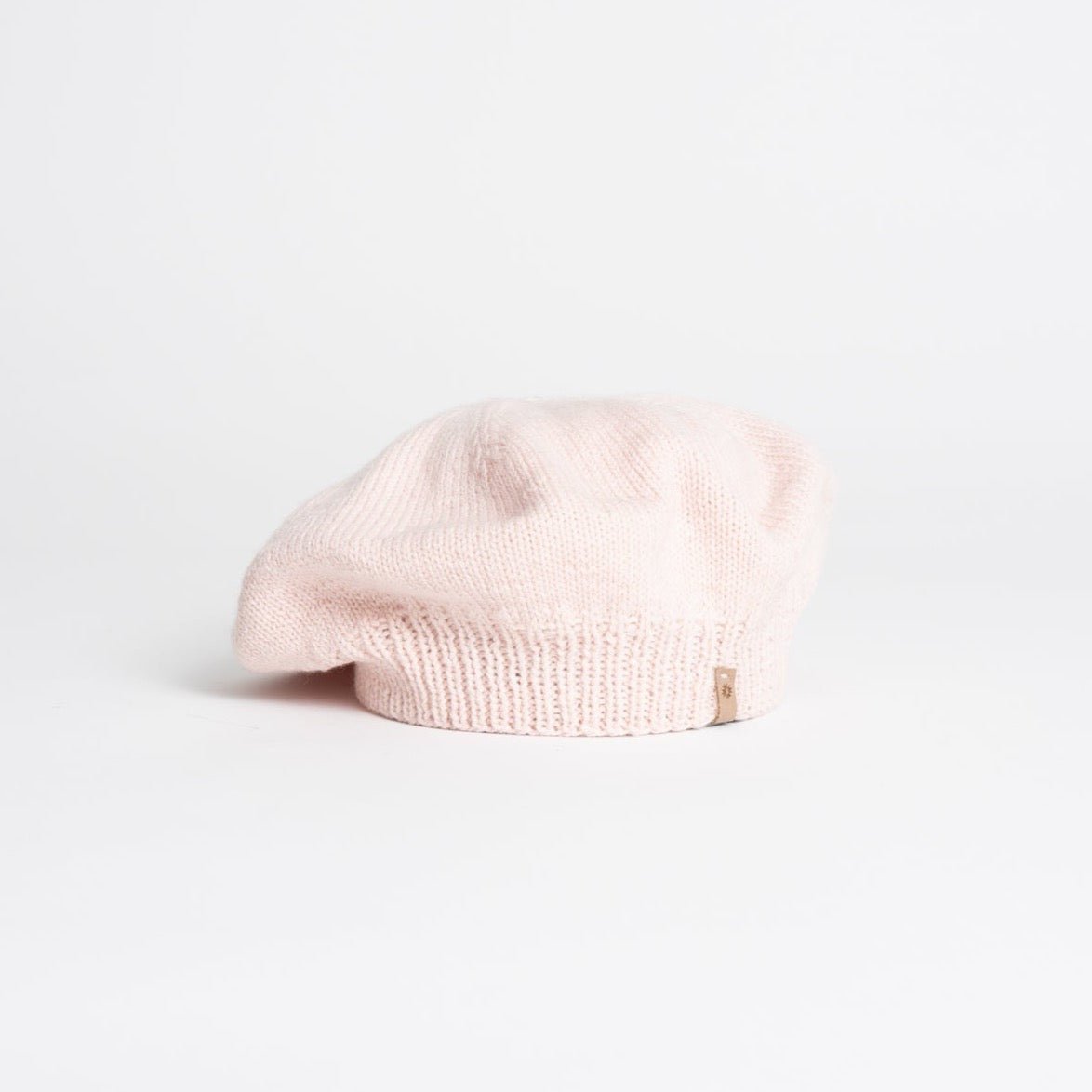 A light pink beret sits against a white background. The Merino Handknit Beret in Blush pink is designed by Dinadi and hand knit in Nepal.