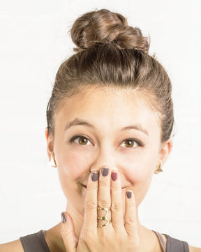 Model whimsically holds hand up to face to show off the size and style of the gold organic triangle ring by betsy & iya.
