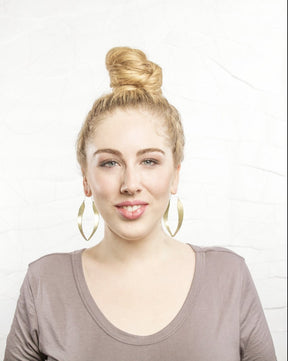 A woman wears the betsy & iya two captains hoops next to a simple background to show size of hoops.