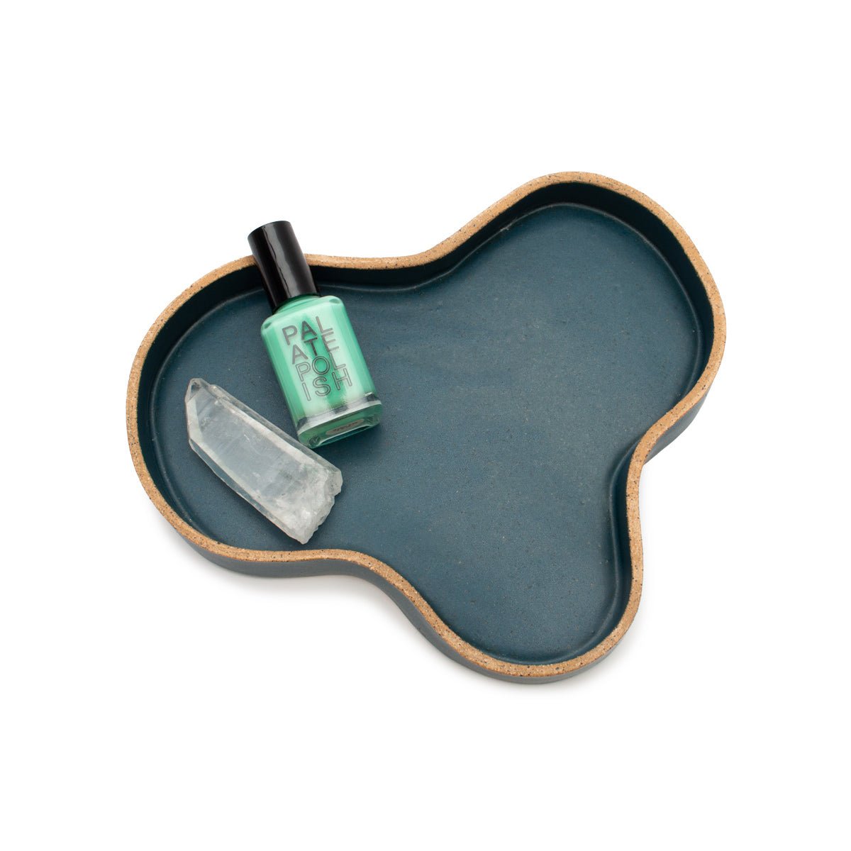 A blob tray holding a bottle of nail polish and a quartz crystal. The Blob Tray in Blue is designed and handmade by Kohai Ceramics in Portland, OR.